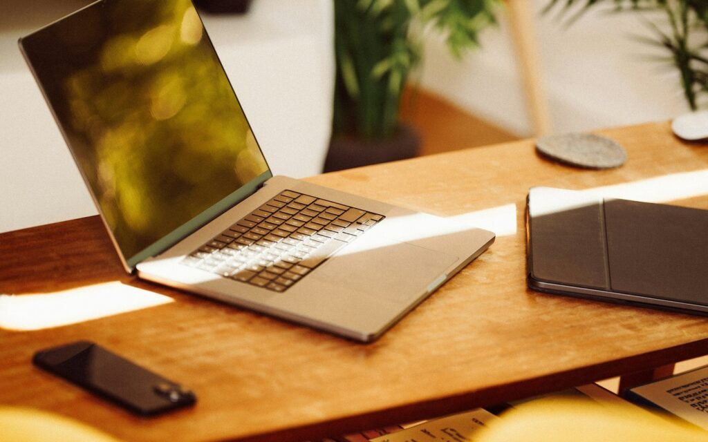A laptop, tablet and phone arranged on a warm wooden product workspace.